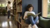 Copil citind singur prima carte într-un colț luminos de bibliotecă